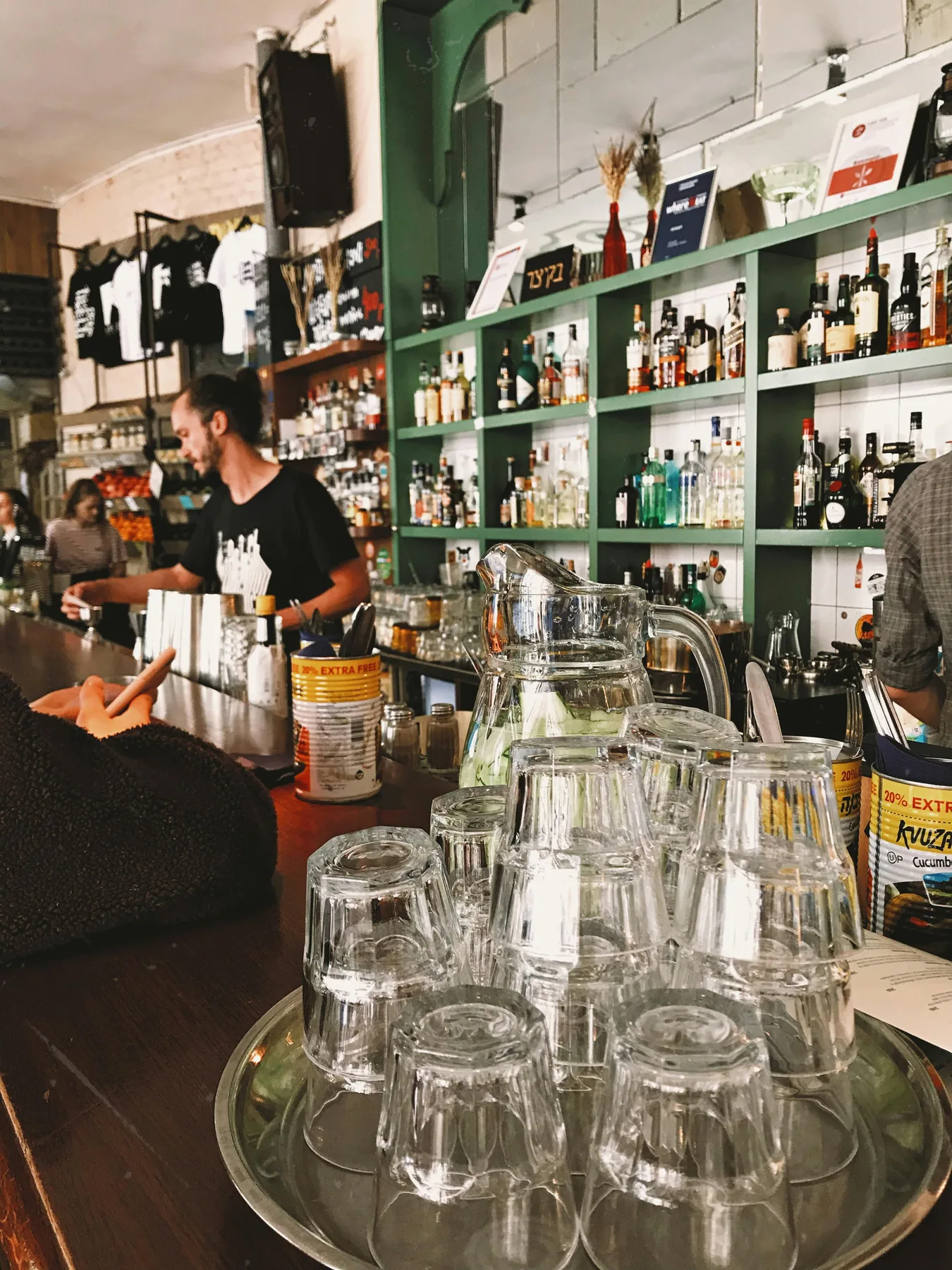 A bartender working behind a stocked bar with a tray of upturned glasses in the foreground