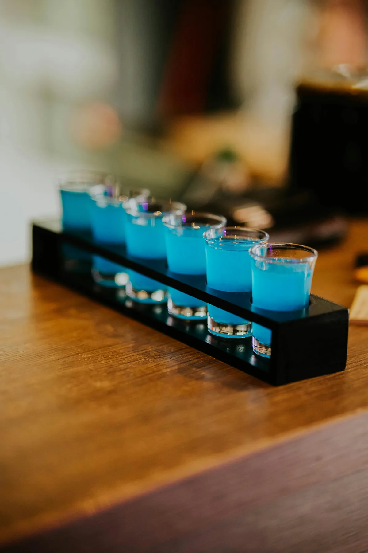 A row of blue shots lined up along a wooden bar top