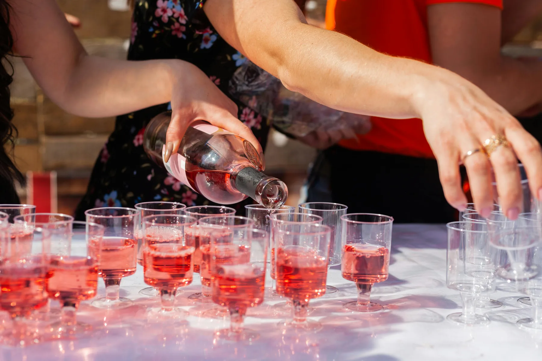 A bottle of rosé being poured into a line of glasses on a white cloth