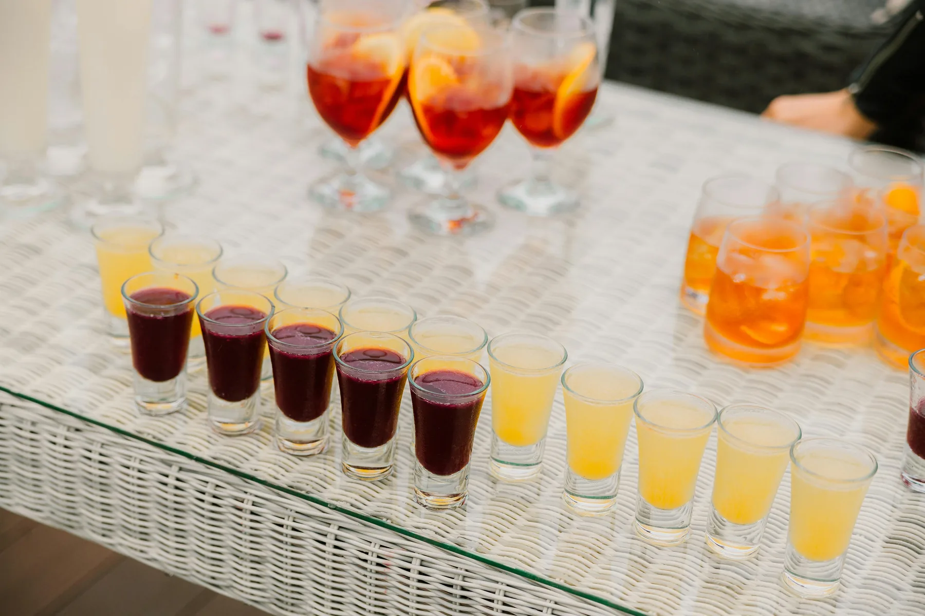 A glass-topped table lined with rows of shots and glasses of sangria at an outdoor party